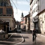A cyclist rides through a charming street in Novi Sad, Serbia, showcasing urban architecture.