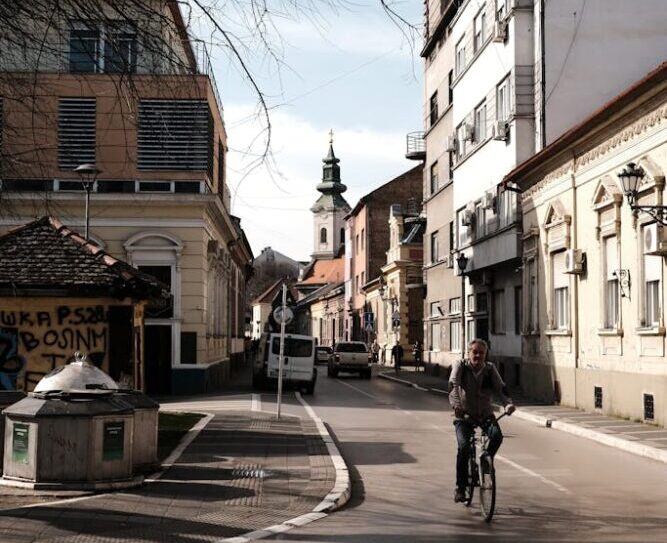 A cyclist rides through a charming street in Novi Sad, Serbia, showcasing urban architecture.
