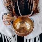 A woman holding a singing bowl, engaging in a peaceful meditation practice.