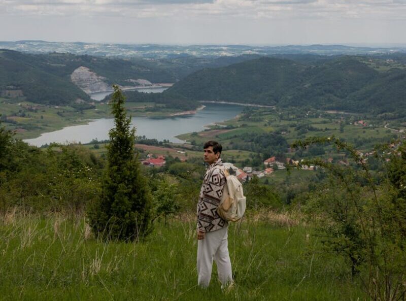 A young man with a backpack takes in the stunning view of the Serbian countryside, symbolizing adventure.