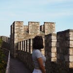 A young woman in striped shirt and white pants stands by the historic stone walls of Kalemegdan Fortress in Belgrade, Serbia.