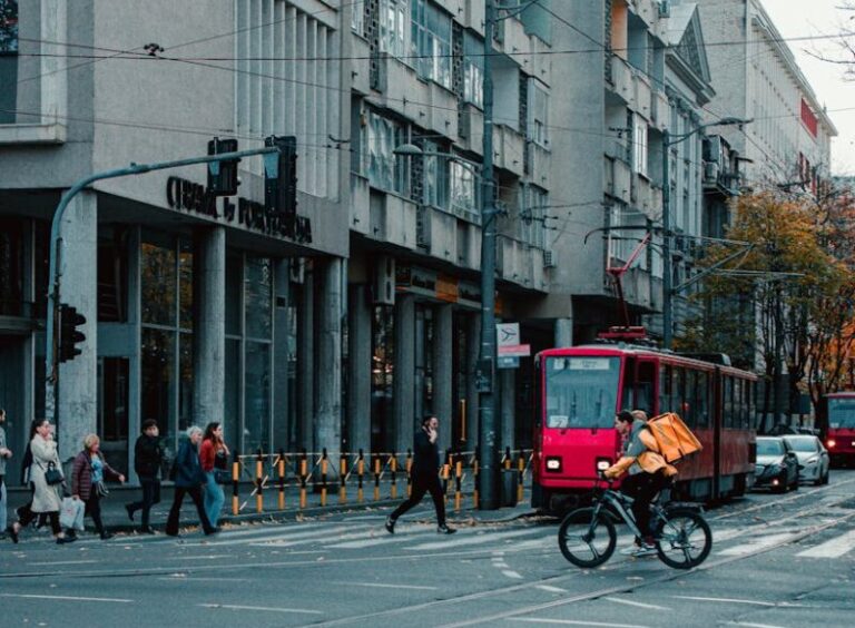 City street view in Belgrade with a red tram and cyclist crossing at an intersection.