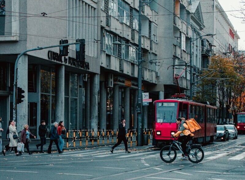 City street view in Belgrade with a red tram and cyclist crossing at an intersection.