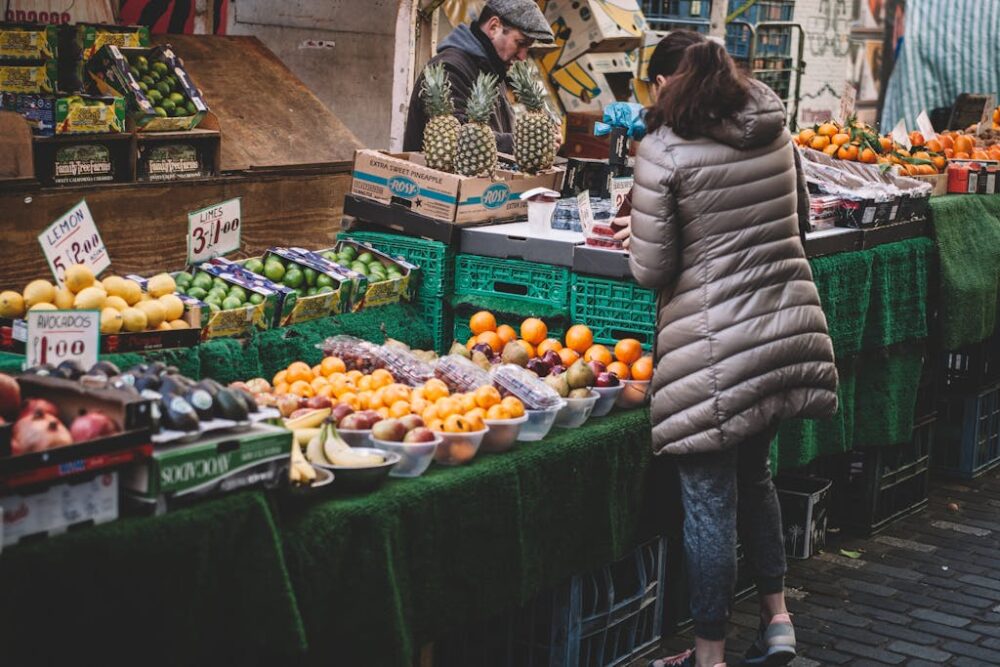 Lively city market stall displaying diverse fresh fruits. A customer browses.