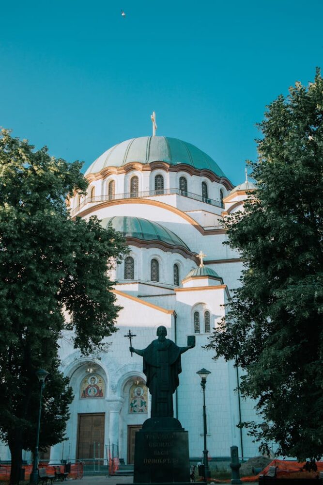 St. Sava Temple framed by lush trees with a clear blue sky in Belgrade, Serbia.