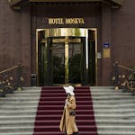 Stylish woman with hat walking past Hotel Moskva's elegant entrance in Belgrade.