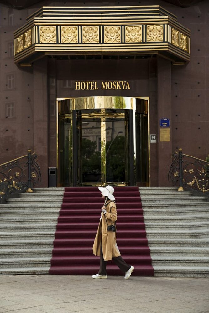 Stylish woman with hat walking past Hotel Moskva's elegant entrance in Belgrade.
