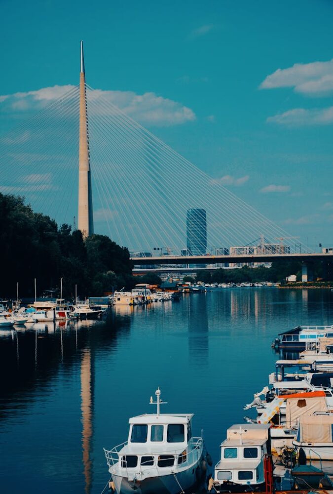 View of Ada Bridge in Belgrade with boats docked on the Sava River under a clear blue sky.